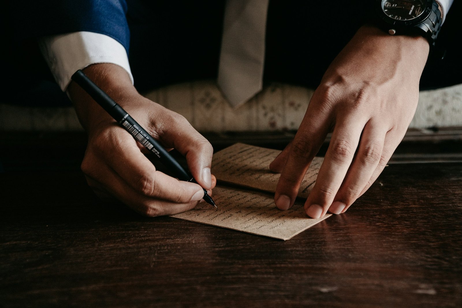 Manos escribiendo una carta sobre una mesa de madera oscura